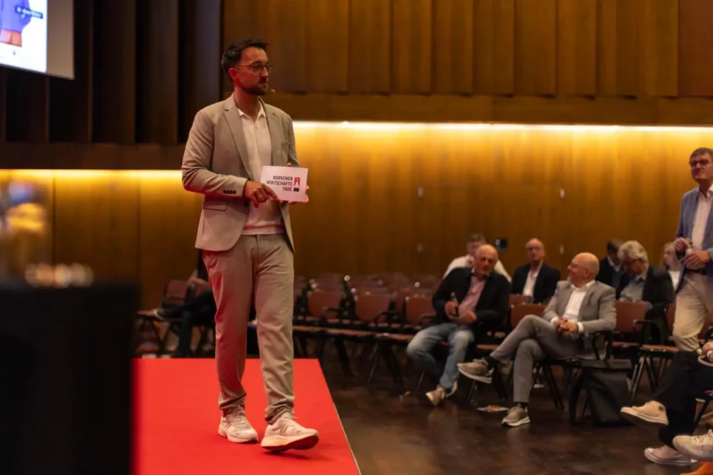 Moderator Phil Dienberg bei einer Podiumsdiskussion vor Publikum in der Halle