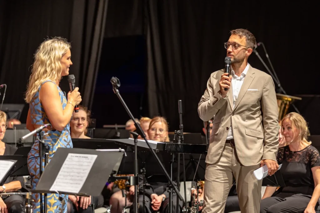 Moderator Phil Dienberg im Gespräch mit einem Gast auf der Bühne vor einem Orchester